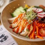 A vibrant salad bowl featuring fresh vegetables and grilled chicken on a wooden table.