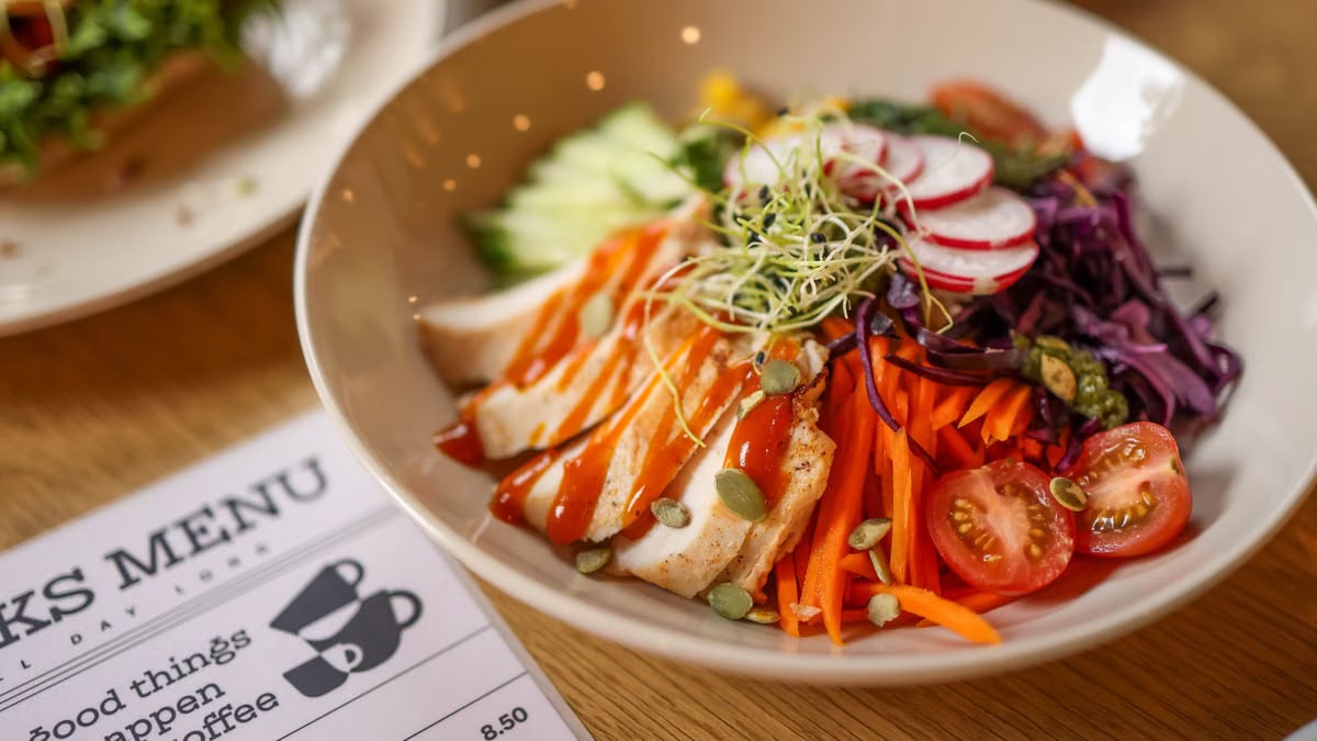 A vibrant salad bowl featuring fresh vegetables and grilled chicken on a wooden table.