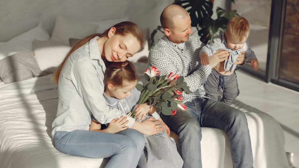 Cheerful parents with children wearing casual clothes smiling while playing with daughter and son in bedroom together during weekend at home